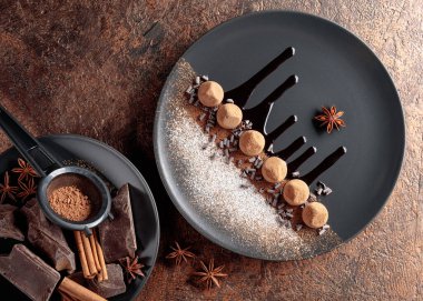 Çikolatalı trüf mantarı, siyah tabakta, çikolata soslu. Tatlılar kakao tozu ve pudra şekerle serpiştirilir. Yakınlarda çikolata, tarçın ve anason parçaları var..