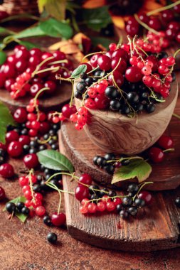 Mutfak masasında vişne, kırmızı ve siyah frenk üzümü. Yapraklarla sulu meyveler.