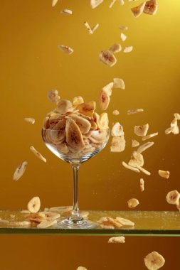 Muz cipsleri cam kaseye düşer. Kopyalama alanı olan sarı arkaplan.