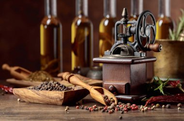 Çeşitli biber ve baharatlar ile Vintage biber değirmeni. Ahşap bir masada pişirme gereçleri, zeytinyağı, baharat ve biberiye şişeleri ile eski biber değirmeni.