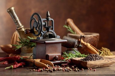 Çeşitli biber ve baharatlı klasik biber değirmeni. Ahşap bir masa üzerinde mutfak aletleri, baharatlar ve biberiye ile eski biber değirmeni. 