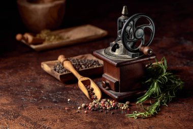 Çeşitli biber ve baharatlı klasik biber değirmeni. Kahverengi arka planda mutfak aletleri, baharatlar ve biberiye olan eski biber değirmeni.