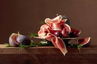 İncirli jambon, biberiye ve eski ahşap bir masada kırmızı zeytin. Boşluğu kopyala.