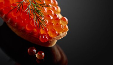 Kırmızı havyarlı kanepe ve siyah yansıtıcı arka planda dereotu. Boşluğu kopyala.