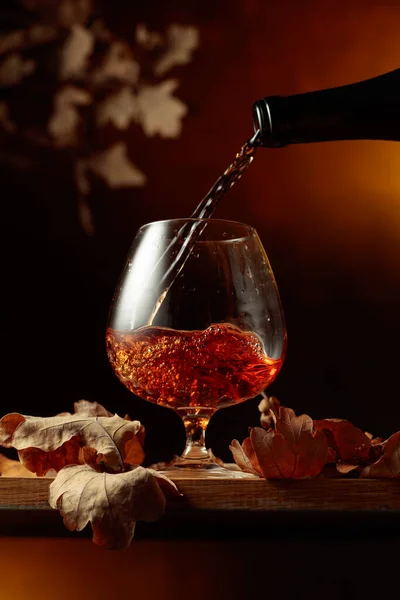 브랜디를 병에서 붓습니다 테이블에 브랜디 냄새마른 나뭇잎 — 스톡 사진