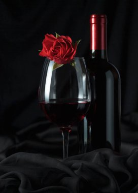 Siyah arka planda kırmızı güllü bir şişe ve bir bardak kırmızı şarap..