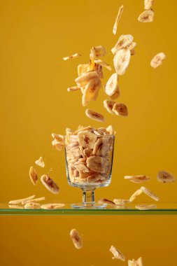 Sarı arka planda cam bir kasede muz cipsi.. 