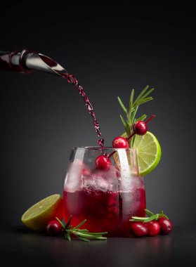 Böğürtlen, limon ve biberiyeyle süslenmiş yabanmersini kokteyli. Buzlu dondurulmuş bardakta kızılcık likörü dökülüyor.. 