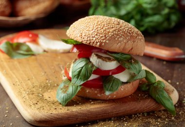 Eski ahşap bir masada mozarella, domates ve fesleğenli sandviç..