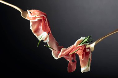 Çatallarda biberiyeli dilimlenmiş prosciutto, siyah arkaplan, kopyalama alanı.