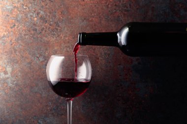 Kırmızı şarap bir şişeden paslı kahverengi arka plandaki bir şarap bardağına dökülür. Metnin için alanı olan ön görünüm.