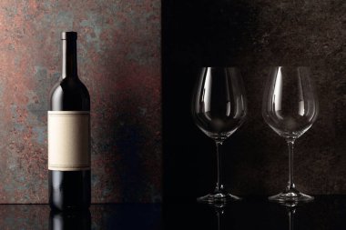  Paslı kahverengi arka planda boş şarap kadehleri olan bir şişe kırmızı şarap. Metnin için alanı olan ön görünüm.