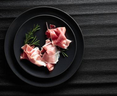 Siyah tabakta Prosciutto ve biberiye. Üst görünüm, alanı kopyala.