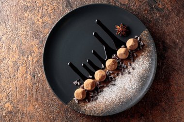 Çikolatalı trüf mantarı, siyah tabakta, çikolata soslu. Tatlılar kakao tozu ve pudra şekerle serpiştirilir. Üst görünüm. 