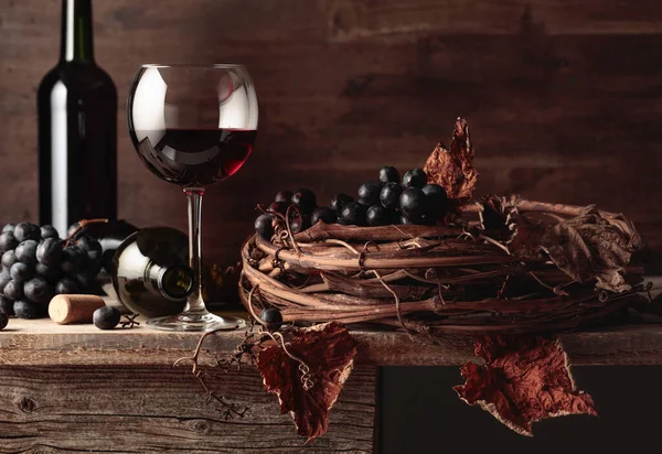 玻璃杯和一瓶红葡萄酒和葡萄放在一张破旧的木制桌子上 — 图库照片