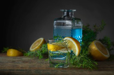 Eski ahşap bir masada mavi cin, tonik ve limonlu kokteyl. Limon dilimleri ve ardıç dallı alkollü içecek..