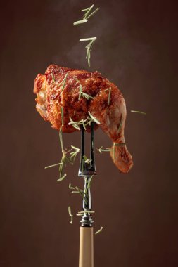 Koyu kahverengi arka planda biberiye serpilmiş ızgara tavuk bacağı. Çataldaki tavuk budu..