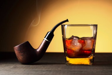 Doğal buzlu bir bardak viski ve ahşap bir masada eski bir pipo..