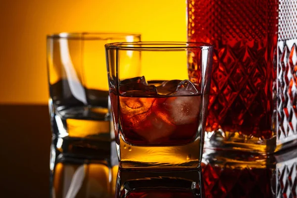 反射的な背景に氷とウイスキーのデカンターとグラス — ストック写真