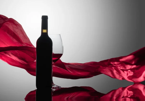 反射的な背景に赤ワインのボトルとグラスです 背景の赤い布のフラッター — ストック写真