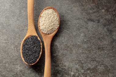 Arkaplanda siyah beyaz susam tohumları olan tahta kaşıklar. Üst görünüm.