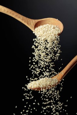 Tahta kaşıklarla susam taneleri dökülür. Siyah arka planda beyaz susam. Boşluğu kopyala.