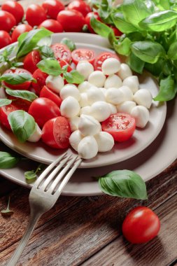 Domatesli mini mozzarella ve eski ahşap bir masada yeşil fesleğen..