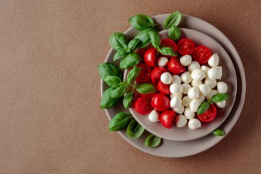 Domatesli Caprese salatası, kahverengi arka planda mini mozzarella ve fesleğen. İtalyan yemeği ve sağlıklı vejetaryen diyeti. Boşluğu kopyala, üst görünüm.