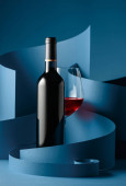 Láhev a sklenice červeného vína na modrém pozadí.