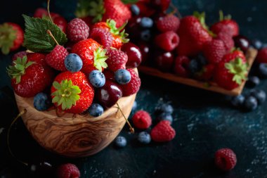 Berries close-up colorful assorted mix of strawberry, blueberry, raspberry and sweet cherry on a dark blue table.