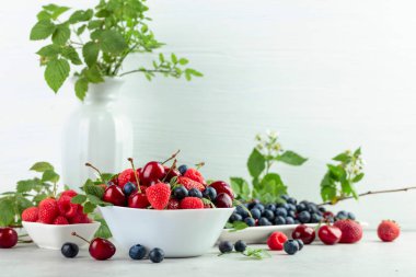 Various fresh berries on a white wooden table. Strawberries, blueberries, raspberries, and cherries are presented.