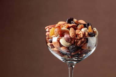 Kahverengi arka planda cam bir kasede fındık ve kuru üzüm karışımı..