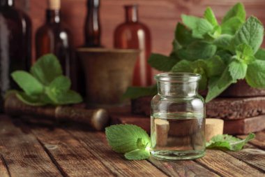 Taze nane yaprakları ve içinde nane yağı bulunan küçük bir şişe. Eski ahşap bir arka planda bitkisel ilaçlar var..