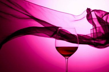 Sallanan saten perdenin arkasında bir kadeh kırmızı şarap. Mor arka plan.