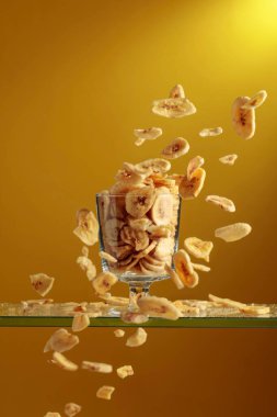 Muz cipsleri cam kaseye düşer. Kopyalama alanı olan sarı arkaplan.