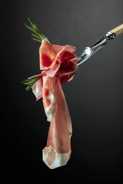 Çatalda biberiyeli dilimlenmiş prosciutto, siyah arka plan..