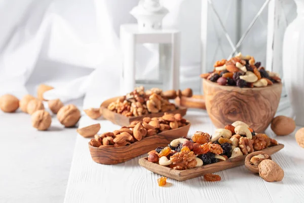 Mix of nuts and raisins on a white wooden table. Presented raisins, walnuts, hazelnuts, cashews, pecans, and almonds.