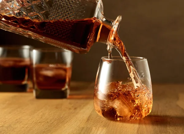ウイスキーは天然氷で傷んだガラスに注ぎ込まれる オークのテーブルの上にウイスキーのグラス — ストック写真