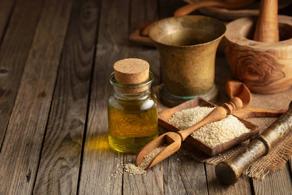 Sesame seeds and oil. Sesame oil with kitchen utensils on an old wooden table.