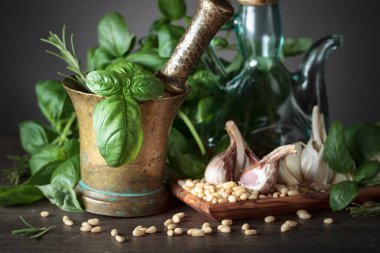 Ahşap bir masada pesto malzemesi. Zeytin yağı, sarımsak, yeşil fesleğen ve çam fıstığı ile eski bakır havan. .