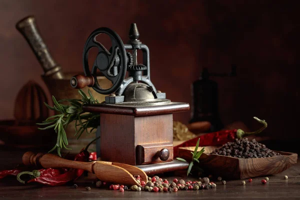 Çeşitli biber ve baharatlı klasik biber değirmeni. Ahşap bir masa üzerinde mutfak aletleri, baharatlar ve biberiye ile eski biber değirmeni. 
