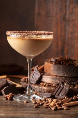 Eski ahşap arka planda buzlu bir bardakta İrlanda kreması ve kahve kokteyli. Kahve çekirdekleri, tarçın, anason ve çikolata parçaları masaya saçıldı.. 