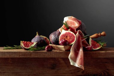 İncirli jambon, biberiye ve eski ahşap bir masada kırmızı zeytin. Boşluğu kopyala.