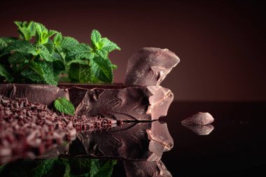 Siyah yansıtıcı arka planda naneli koyu acı çikolata ve çikolata parçaları. Boşluğu kopyala.