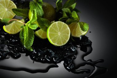 Limon dilimleri, nane yaprakları ve ıslak siyah yansıtıcı arka planda buz parçaları..
