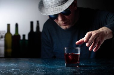 Şapkalı adam buzlu viski içiyor. Seçici odak.