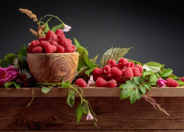 Ahşap kasede ahududu. Yaz ayları ahududu, çayır otları ve eski ahşap bir masanın üzerindeki çiçeklerle geçer. Boşluğu kopyala.