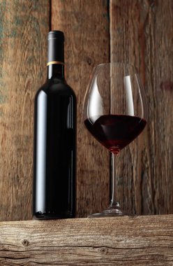 Eski ahşap bir masada şişe ve bir bardak kırmızı şarap. Seçici odak.