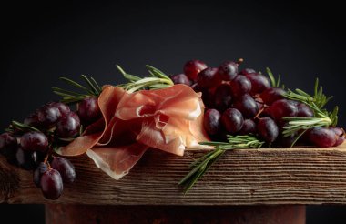 Eski ahşap bir tahtada üzümlü ve biberiyeli jambon..