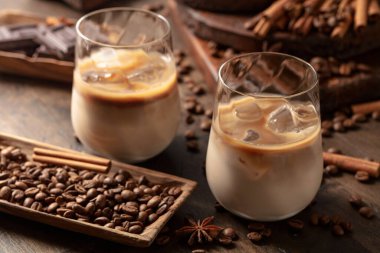 Eski ahşap arka planda buzlu bardakta İrlanda kreması ve kahve kokteyli. Kahve çekirdekleri, tarçın, anason ve çikolata parçaları masaya saçıldı.. 